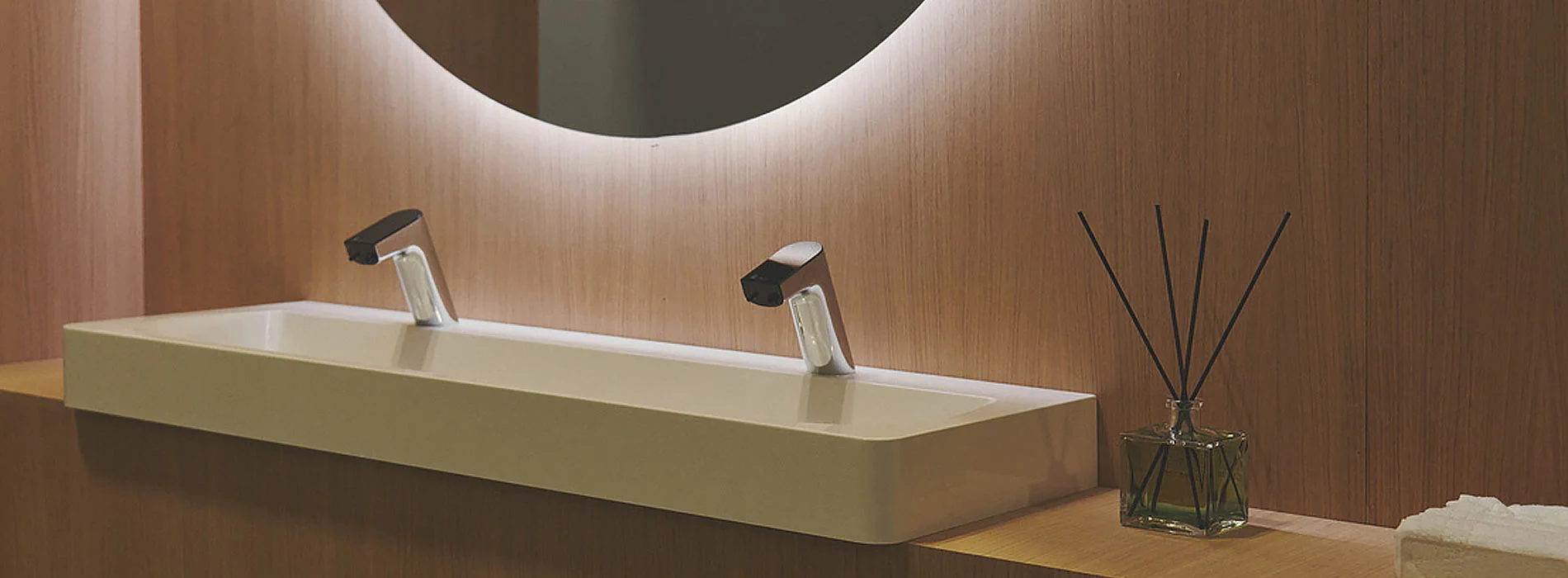 Wall-mounted basin with sensor taps against a warm timber wall